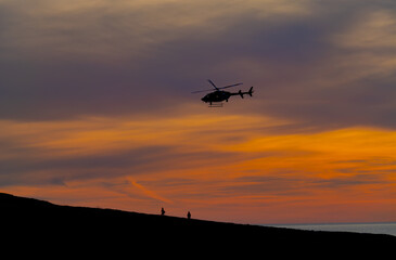 Silhouette of a helicopter flying over hikers on the California coast at sunset