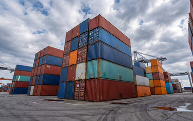 Colorful shipping containers stacked high in a busy port area under a cloudy sky. Industrial scene showcases logistics and transportation within modern commerce.