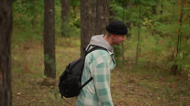 caucasian wanderer touching young sapling in pine forest, backpack carried, inspecting leaves with gentle hand, sensory grounding practice, calm mossy floor and warm dappled light, intimate nature