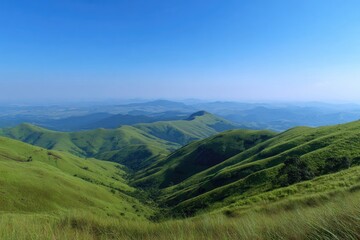 Obraz premium Lush green hills roll towards distant mountains under a clear, bright blue sky