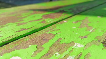 Worn Paint on Wooden Surface: Close-up details of a weathered wooden surface, revealing peeling bright green paint and a hint of the wood grain beneath.