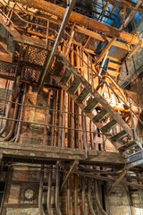 An aged industrial interior with metal stairs, pipes, and framework that show signs of wear. The...