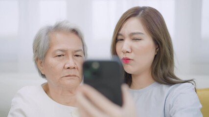 Young Asian woman and mather looking stressed and concerned while checking a suspicious alert or fake news on her smartphone, representing digital fraud awareness and cybersecurity stress at home.