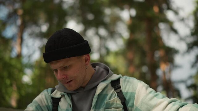 white hiker reads large map in forest, unfolding paper among pine trees, scanning contours and compass, plotting route and checking direction, introspective scout smoothing creased sheet