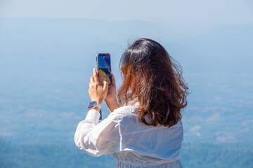 A woman uses her smartphone to take pictures of the sunrise in a valley with abundant nature tourism and technology.