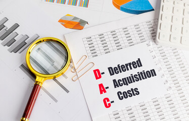 Deferred acquisition costs abbreviation on paper with financial documents, magnifying glass and calculator