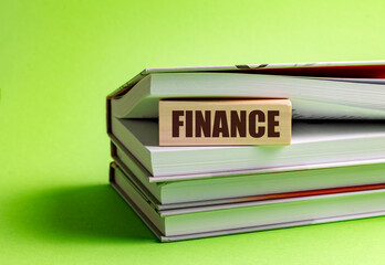 Finance concept shown on wooden block between stacked books on green background