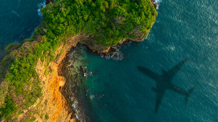 Aerial view of a dense, vibrant green coastal jungle meeting dark blue ocean water. A thin, rocky beach and white foamy waves separate the rugged terrain from the sea.concept nature	