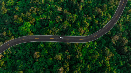 Aerial view of dark green forest road and white electric car Natural landscape and elevated roads Adventure travel and transportation and environmental protection concept	
