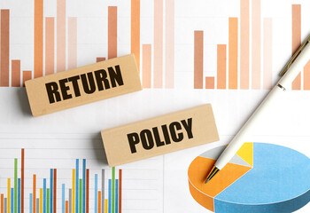 Return policy words on wooden blocks placed over financial charts with pen
