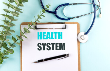 Health system phrase on clipboard with stethoscope, pen and green plant on blue background