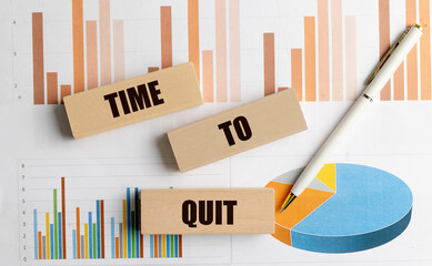 Time to quit phrase on wooden blocks over business charts with pen on desk