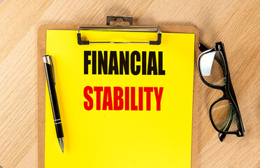 Financial stability phrase on yellow clipboard with pen and eyeglasses on wooden table
