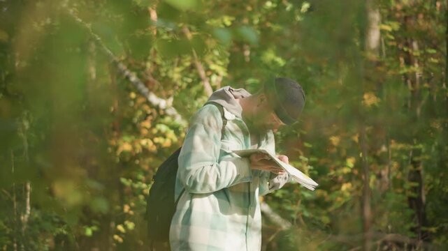 White male hiker in sunlit forest scanning map, solo backpacker assessing route, amateur cartographer checking bearings, nature observer pausing beneath canopy, quiet reflective mood with golden