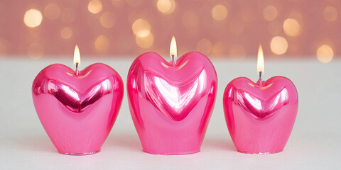 Heart-shaped pink candles glowing softly on blurred background  