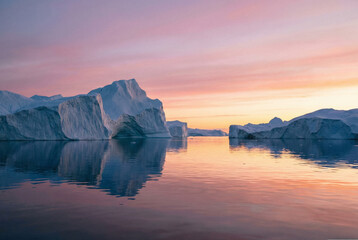 Large icebergs floating in Disko Bay illuminated by the colorful pink and orange light of the Arctic midnight sun