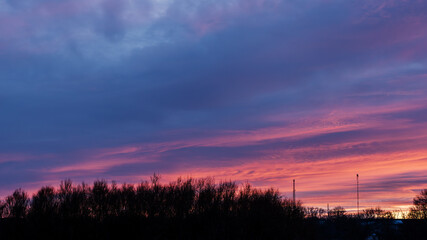 Colorful dramatic sunset sky with layered clouds over dark forest silhouettes
