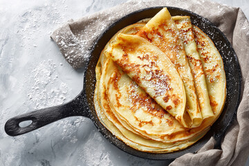 delicious stack of crepes sprinkled with powdered sugar in a cast iron pan