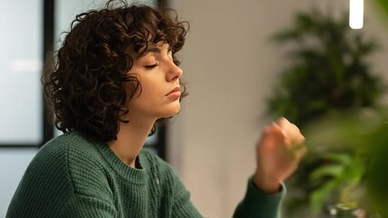 Young Woman with Curly Hair Looking Pensive in a Cozy Indoor Setting Surrounded by Greenery