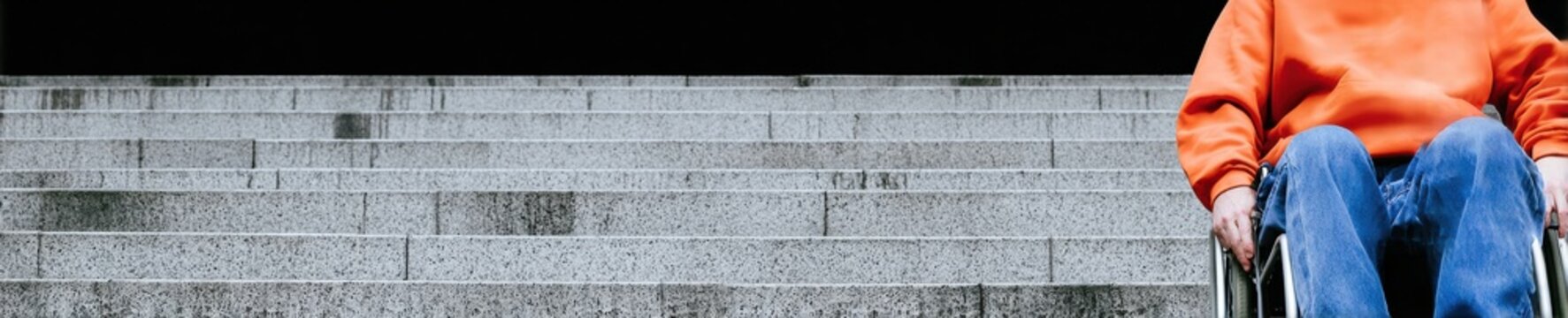 Person in manual wheelchair at base of steep concrete staircase, representing architectural barriers and limited accessibility for urban planning brochures