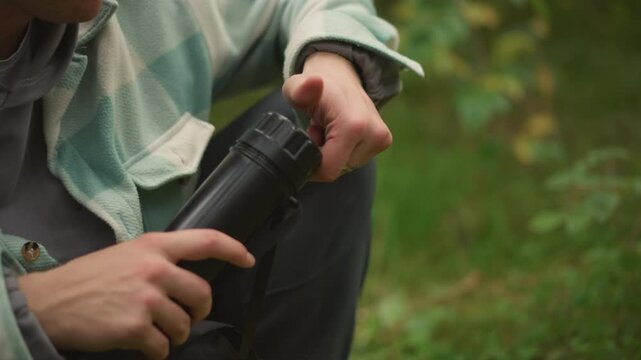 white camper retrieves yellow thermos, inspects monocular lens and extends spotting tube, then scans distant canopy relaxed exploration vibe, camp pause and subtle nature observation on trail