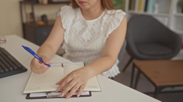 Woman holding pen above open planner notebook at office building desk, hands on pages writing gesture; concentration routine.