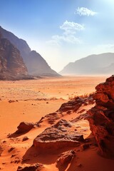 Fototapeta premium Expansive desert landscape, reddish sand, rocky outcrops, hazy mountains in background under a mostly clear sky