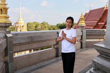 Peaceful Asian woman wearing white clothes standing with hands in prayer inside a Buddhist temple, expressing faith, spirituality, and cultural tradition
