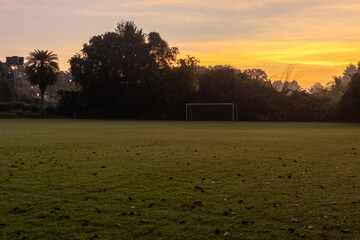 Quiet football field at sunrise with warm golden light, morning sky, and peaceful atmosphere, ideal for sports and outdoor background use.