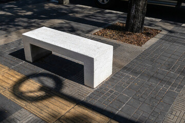 Concrete bench placed beside a public sidewalk, representing urban design, street furniture, public space, and everyday city life in an outdoor environment.