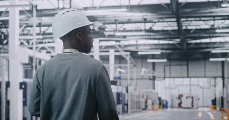 African American Adult Professional Engineer Walks at Head of Vast, Clean Automated Plant, Wearing Hard Hat. Concept of Physical Presence and Direct Control Over Complex Modern Robotic Systems. - Powered by Adobe
