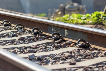 Close-up of railway track with steel rail, fasteners, and gravel ballast, showing transportation infrastructure detail and industrial outdoor setting.