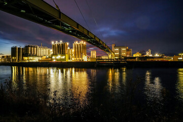 The Gersthofen industrial park at night. A chemical and industrial site with futuristic-looking buildings and silos. The green bridge structure spans the Lech Canal.