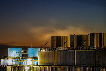 Gersthofen Industrial Park at night. Chemical production facility with large cylindrical silos, pipelines, and steaming emissions into the night sky
