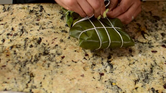 Hands tying hallacas with palm leaves, traditional Venezuelan dish, authentic homemade preparation, festive culinary process, close-up of artisanal cooking.