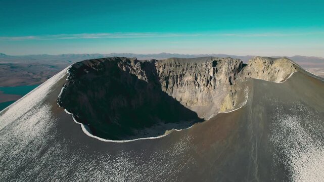 Orbiting drone shot of the Parinacota Volcano crater rim. The snow-capped peak and the vast, arid wilderness of Sajama National Park.