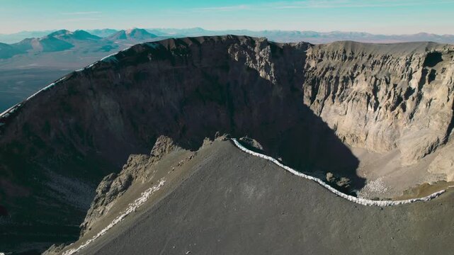 A cinematic orbiting drone shot looking into the rugged summit crater of Parinacota Volcano. Dramatic inner cliffs and expansive views of Sajama National Park.