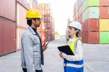 Two industrial workers discussing logistics data on a tablet at a cargo container terminal. A foreman and female engineer manage shipping delivery at a commercial distribution port.
