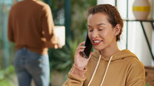 Focus on multicultural woman calling on mobile phone while unrecognizable man getting parcel from courier in background