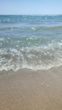 Sea waves with turquoise transparent water rolling on sand of sandy beach on sunny summer day. Quiet calm windless sea. Low angle. From below. Nobody. Nature backdrop. Natural background Vertical