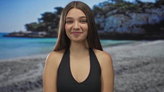 Teenage girl wearing black tank top and silver bracelets clasps hands and smiles with tanned shoulders in studio; serenity.