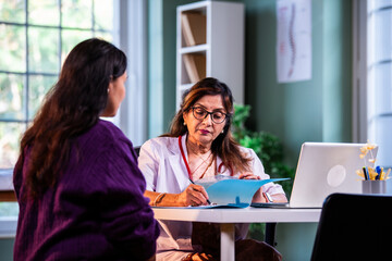 Experienced Indian woman doctor consulting young beautiful patient with case file