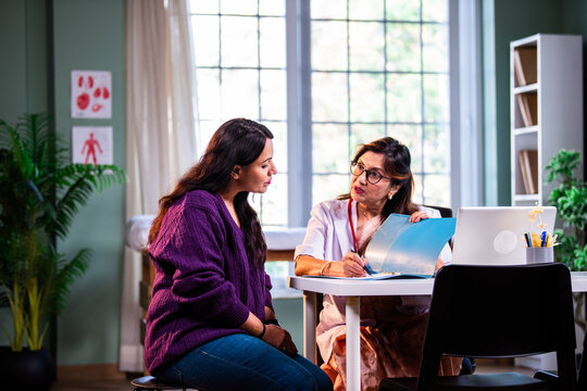 Experienced Indian woman doctor consulting young beautiful patient with case file