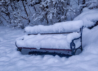 A peaceful winter scene featuring an empty park bench covered in a thick layer of fresh snow