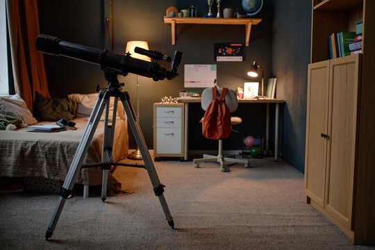 No people shot of telescope in bedroom of child prodigy studying astronomy demonstrating scientific curiosity and advanced knowledge, desk with computer and educational materials visible in background - Powered by Adobe