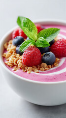 Pink yogurt bowl topped with granola, blueberries, raspberries and mint on a clean white background. Healthy breakfast, fresh food styling and vegetarian snack concept.