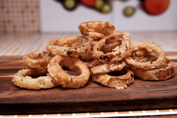 Naklejka premium Homemade crunchy fried onion rings on wooden board. Making onion ring homemade. Homemade food, snack, and fast food preparation concept.