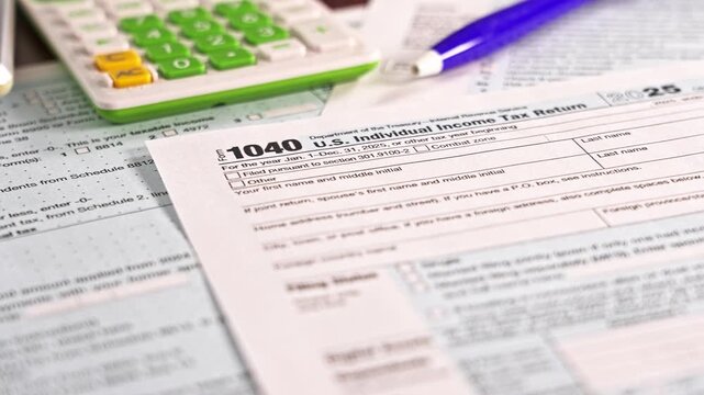 A person completes their U.S. individual income tax return 1040 form using tax forms, a calculator, and a pen. The desk is organized with papers and tools for tax and preparation camera is in motion