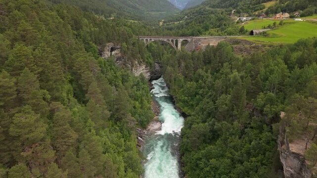 A Stone Arch Bridge Crosses a Forested Gorge Above a Rushing River at Kylling Bridge, Along the Raumabanen in Norway - Aerial Drone Shot