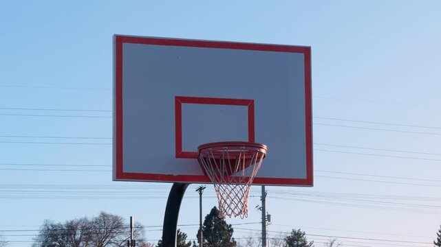 Slow panning shot of an outdoor basketball hoop and backboard under a clear blue sky